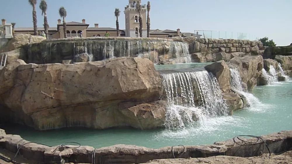 Rock waterfall cascading into a turquoise pool in front of the Jumeirah Golf Estates club house