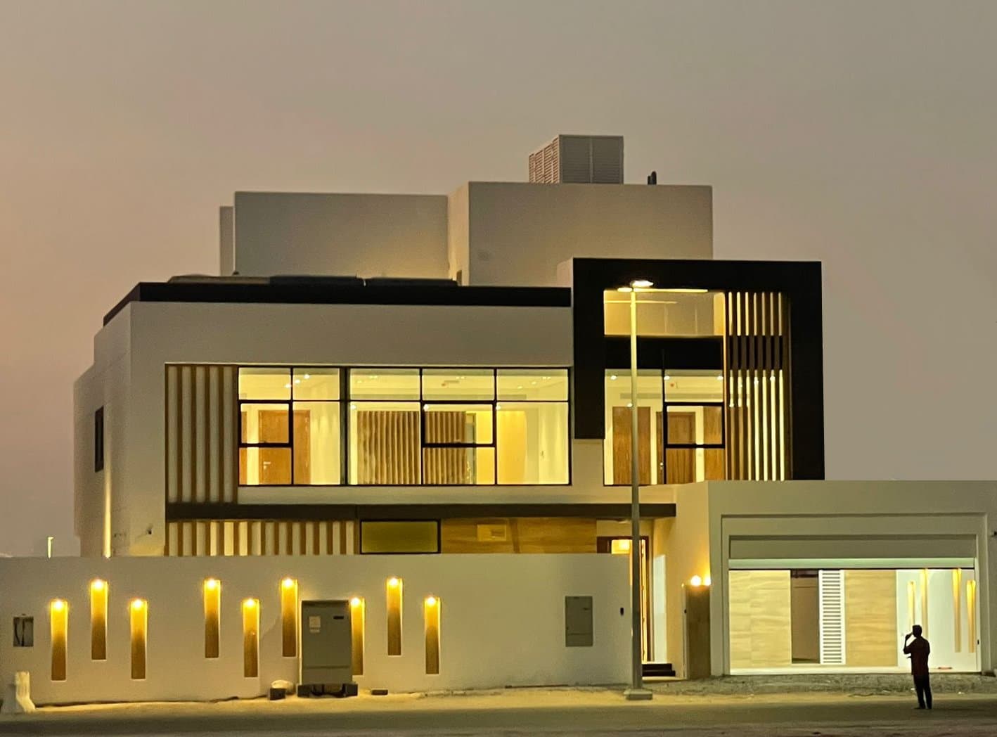 Modern two-storey villa at dusk with warm lighting behind full-height glazing and timber screens